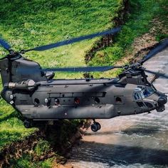 the helicopter is flying low to the ground above the water and green grass on the bank