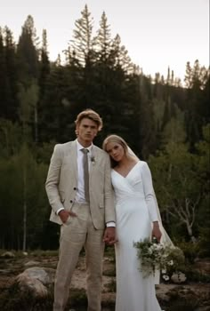 a man and woman in wedding attire standing next to each other with trees in the background