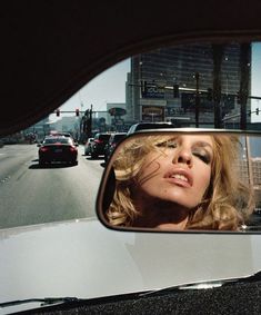 a woman's face is reflected in the rear view mirror of a car on a city street