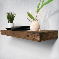 a wooden shelf with plates and vases on it, next to a green plant