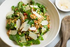 a salad in a white bowl with parmesan cheese and lettuce on top