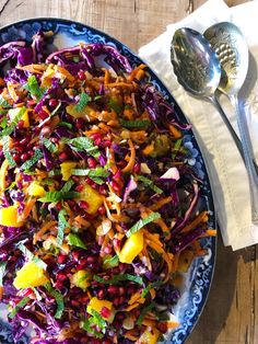 a salad with carrots, cabbage and other vegetables on a blue plate next to a spoon