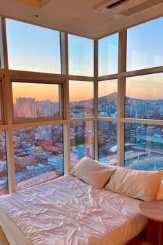 a bed sitting in front of large windows next to a wooden table with a lamp on it