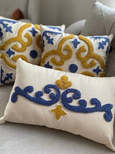 three decorative pillows on a bed with blue and yellow trimmings, one in the shape of a crown