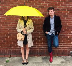 two people standing next to each other with an umbrella in front of a brick wall