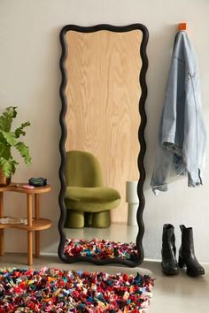 a mirror sitting on top of a wooden floor next to a green chair and potted plant