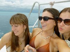 three women in bikinis on a boat drinking wine and looking at something off to the side