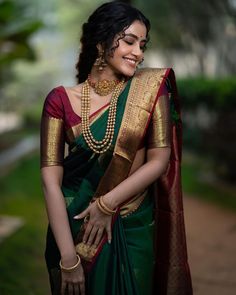 a woman in a green and gold sari with pearls on her neck, smiling at the camera