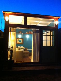 the inside of a tiny house with lights on and curtains open at night, outside