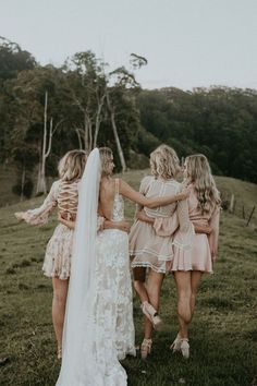 three bridesmaids are walking in the grass with their arms around each other and one is wearing a wedding dress