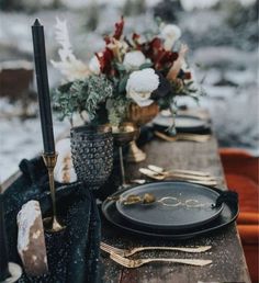 a table set with black plates and goldware