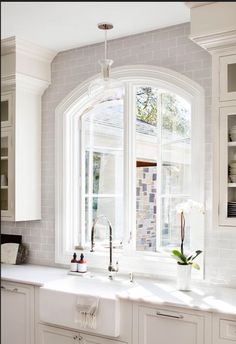 a white kitchen with an arched window, sink and dishwasher on the counter