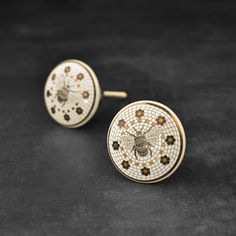 small white and brown mosaic bee studs on black velvet surface with gold colored accents