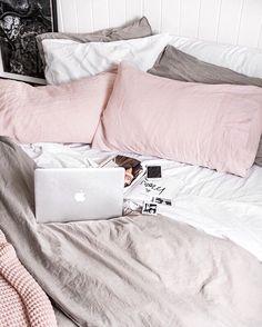 a laptop computer sitting on top of a bed next to pink and gray pillows,