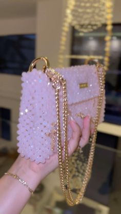 a hand holding a pink purse with gold chains