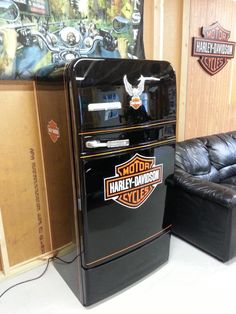 an old harley davidson refrigerator sitting next to a black leather couch in a room with wood paneling