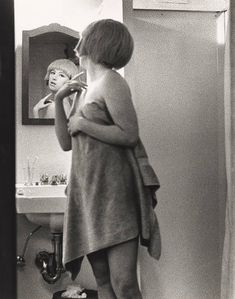 a woman standing in front of a mirror brushing her teeth and looking at herself in the mirror