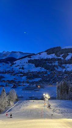 a ski slope with snow covered mountains in the background and people skiing on it at night