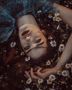 a woman laying on the ground with her face covered by flowers