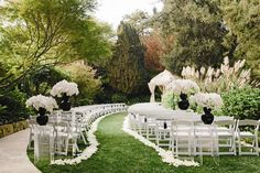 an outdoor ceremony setup with white chairs and black vases on the aisle, surrounded by flowers