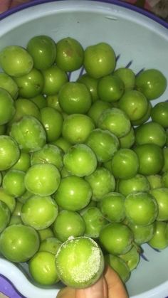 green apples are in a blue and white bowl, being held by someone's hand