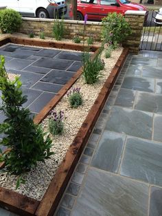 an outdoor garden with gravel and plants in the center, next to a red car