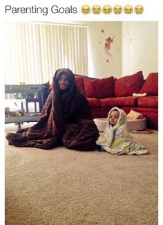 a woman sitting on the floor next to a child wearing a blanket and holding a laptop