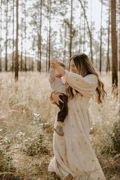 a woman holding a baby in her arms while walking through a field with tall grass