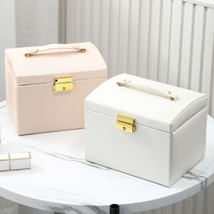 two white boxes sitting on top of a table next to each other with gold handles