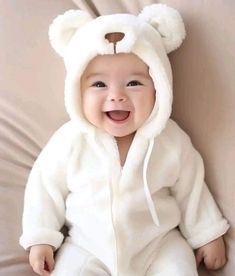 a baby wearing a white bear suit sitting on top of a bed with its mouth open