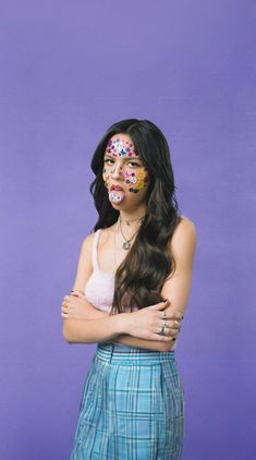 a woman with her arms crossed and painted in different colors, standing against a purple background