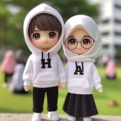 two dolls are standing next to each other in front of some grass and trees, one is wearing a white hoodie with black letters on it