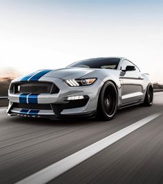 a silver mustang with blue stripes driving down the road