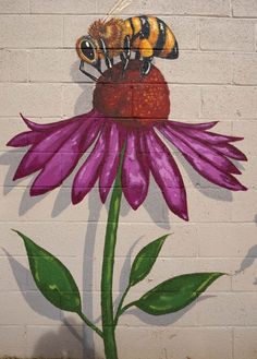 a painted mural of two bees on a purple flower with green leaves in front of a white brick wall