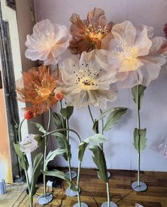 three vases filled with flowers sitting on top of a wooden floor next to a wall