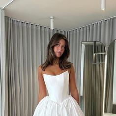 a woman standing in front of a mirror wearing a white dress