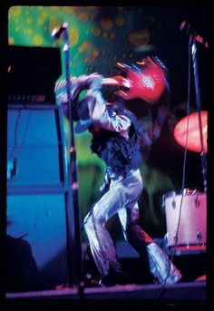 a man standing on top of a stage next to a microphone and drum set in front of him