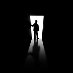 a man standing in the doorway of a dark room with his hand out to someone