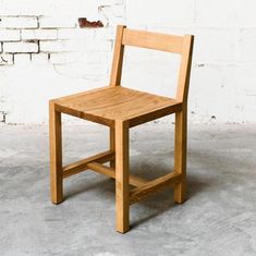 a wooden chair sitting in front of a white brick wall on concrete floored area