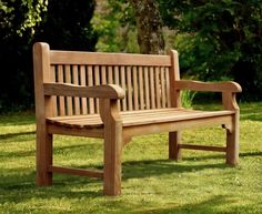 a wooden bench sitting on top of a green grass covered park field with trees in the background