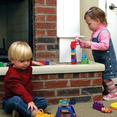 two children playing with toys in front of a fireplace