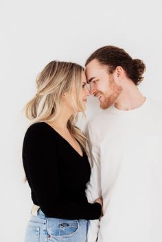 a man and woman standing next to each other in front of a white wall smiling