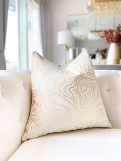 a close up of a white couch with a pillow on it's back and a mirror in the background