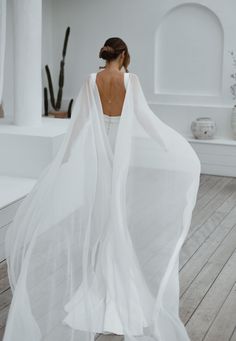 the back of a woman wearing a white dress with sheer, flowing fabric on it