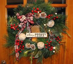 a christmas wreath with pine cones, berries and evergreens hanging from the front door