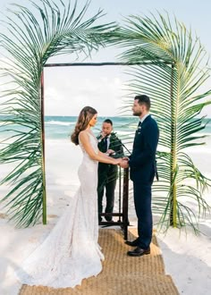 a bride and groom standing under a palm tree on the beach during their wedding ceremony