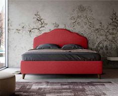 a red bed sitting in the middle of a bedroom next to a wall with flowers on it