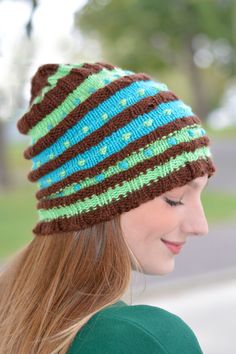 a woman wearing a knitted hat with green and brown stripes on it's brim