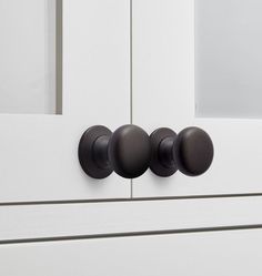 three black knobs on a white cabinet door