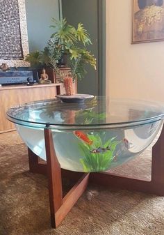 a glass table with fish in it on carpeted floor next to wall and potted plant